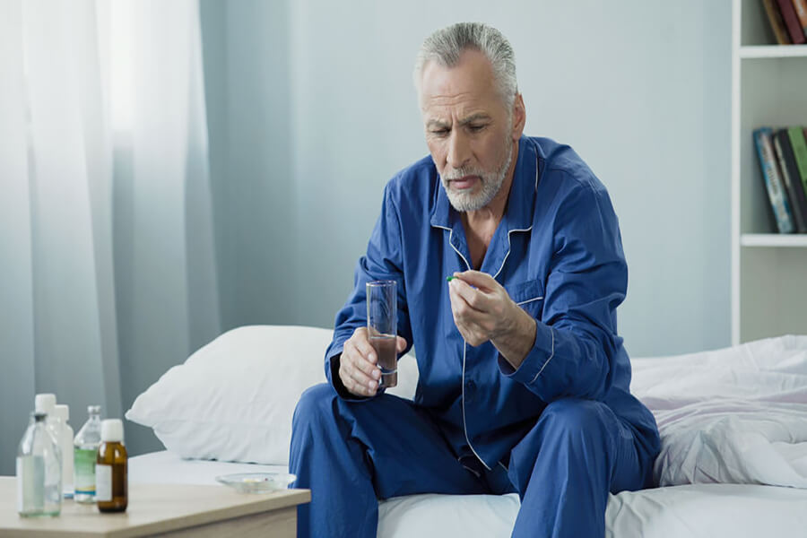 Older male taking pill sitting on bed
