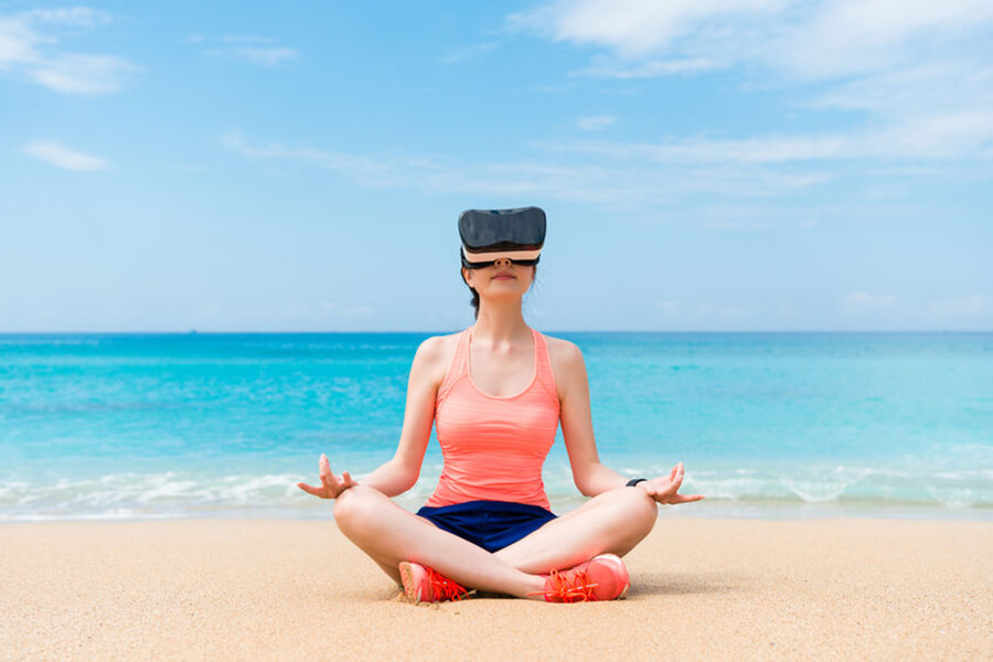 Woman meditating on beach with VR headset