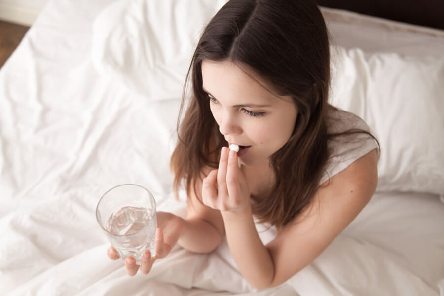 Woman taking pill with water in bed