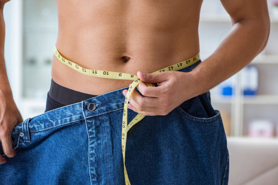 Slim shirtless man holding up measuring tape and jeans