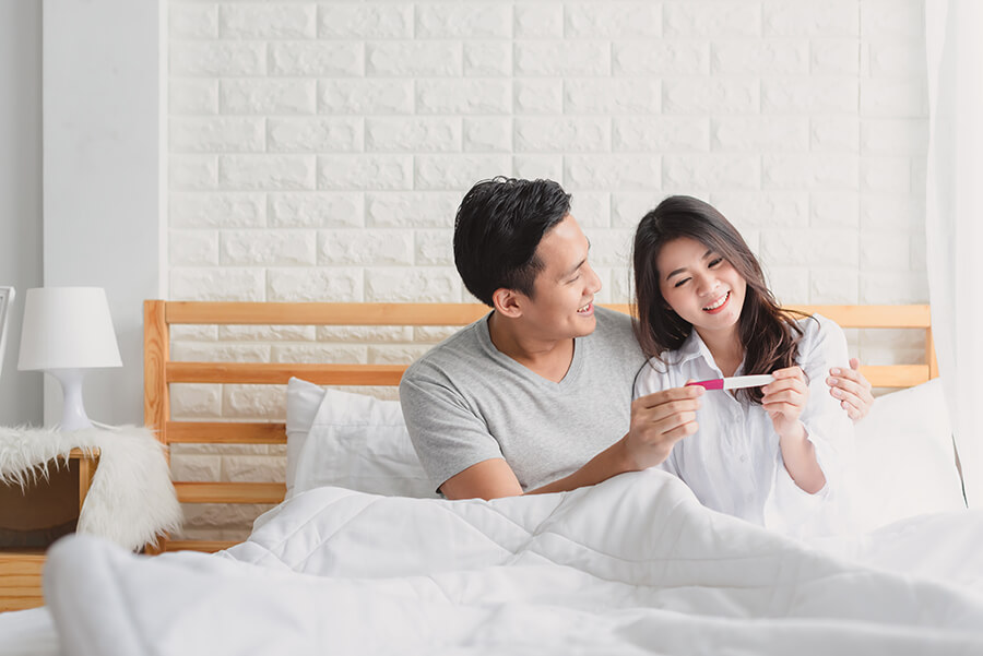 Happy asian couple smiling after find out positive pregnancy test in bedroom at home