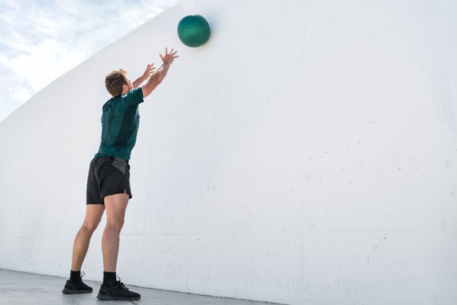 Strength training fit man cross training throwing medicine ball on gym wall at fitness center