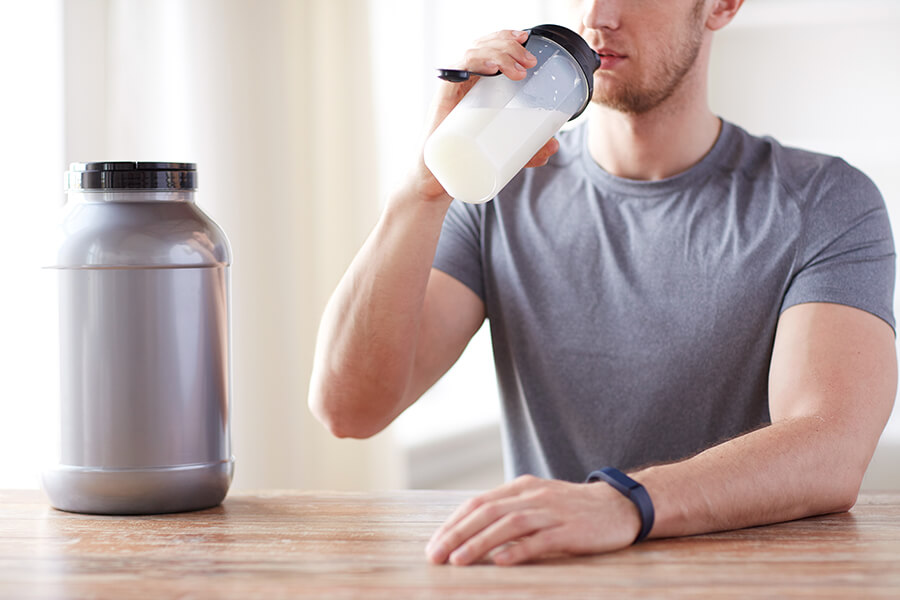 Sport, fitness, healthy lifestyle and people concept - close up of man in fitness bracelet with jar and bottle drinking protein shake
